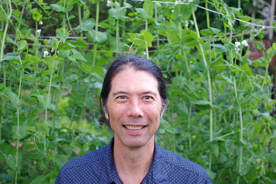Professor of biological science Brian Inouye standing in front of tall plants.