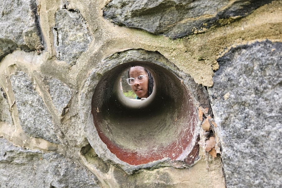 Cole looks through a clay pipe in a stone wall at the gunpowder mill at the Hagley Museum, as part of site visits related to the Vernacular Architecture Forum annual conference in May 2025. Courtesy Photo.