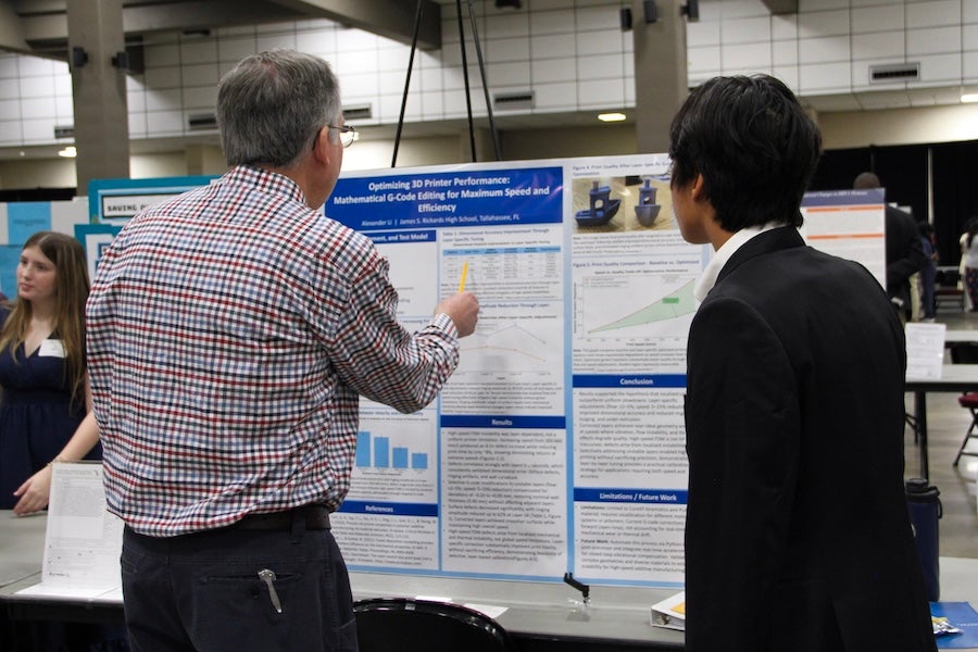 A judge inspects a student's poster at the 2026 Capital Regional Science and Engineering Fair Feb. 13 in Tallahassee, Florida. Photo by Bella Bozied.