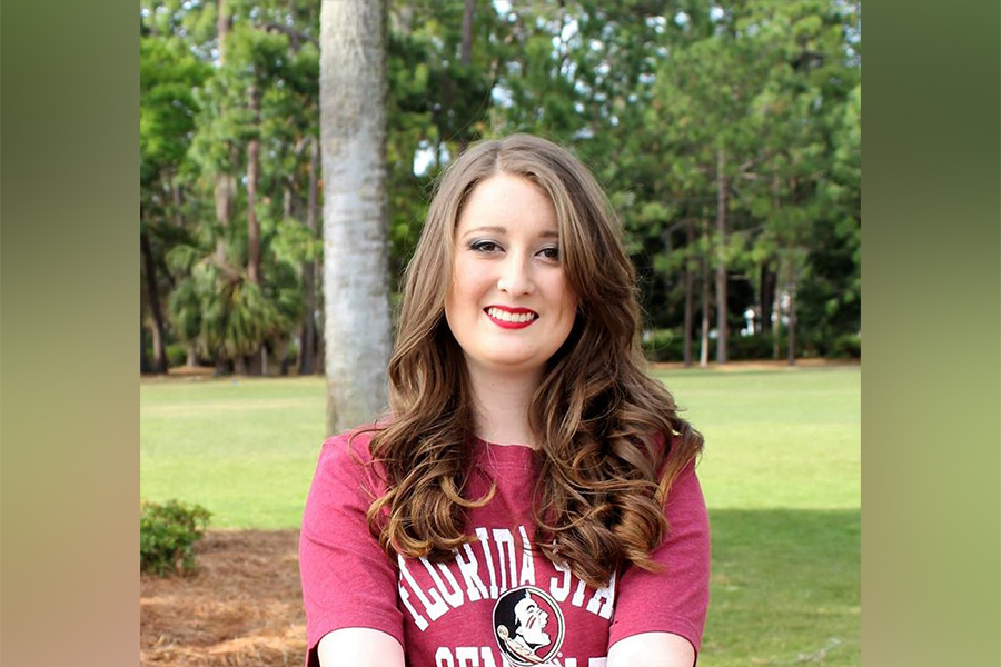 This photo shows a girl with brown, curly hair wearing an FSU shirt as she sits on the ground. 