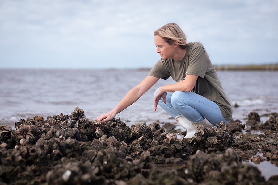 Morgan Hawkins crouching on an oyster reef at the FSU Coastal and Marine Laboratory. Photo by Devin Bittner.