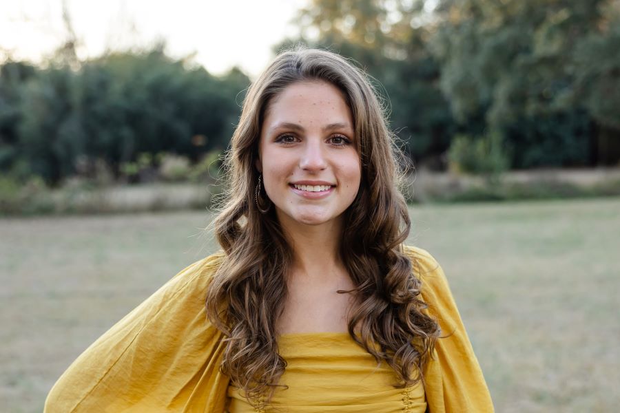 This is a photo of Caroline Sizemore outside in a yellow shirt smiling. 